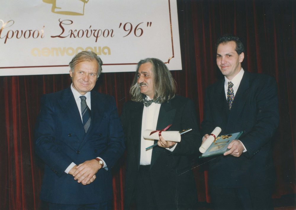 Ισοβαθμία στην τρίτη θέση για την καλύτερη ελληνική κουζίνα του 1996. Μιχάλης Κουμπιάδης(στο κέντρο) για τα «Κιούπια» και Τίμος Πετρίδης για την «Καλλίστη»  παραλαμβάνουν τα βραβεία τους από τον Σπύρο Κοκοτό, Πρόεδρο του ΣΕΤΕ.