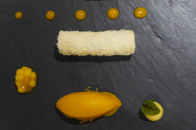 Το ραβανί σε μια conceptual εκδοχή, με κορμό καρύδας, κρέμα μαστίχας και μάνγκο σε τρεις υφές 